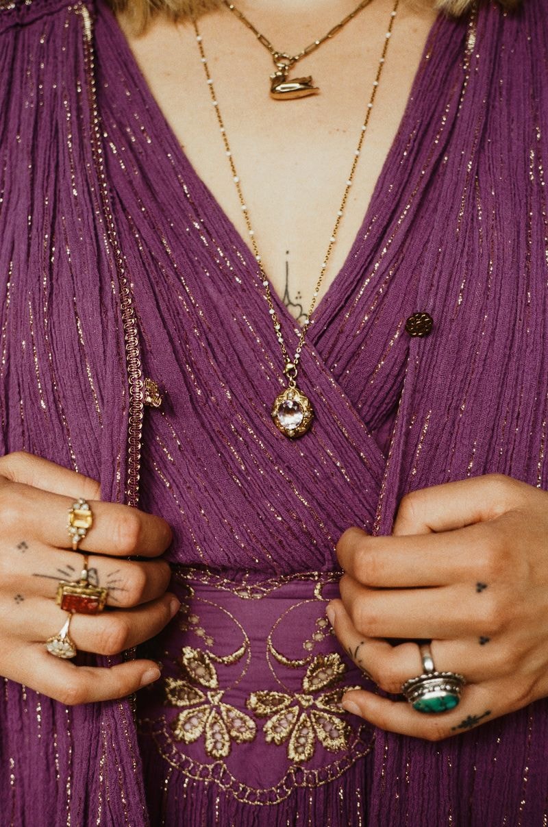 Close-up van paarse jurk met sierlijke ketting en medaillon, omgeven door levendige kleuren