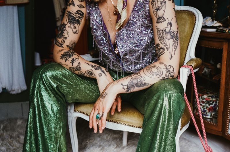 Vrouw in vintage outfit met paarse glittertop, zittend op stoel te midden van kleurrijke circus- en discovibes