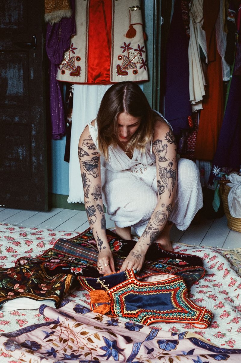 Vrouw in vintage outfit met tatoeages, staand in levendig en creatief atelier in Amersfoort